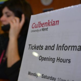 A poster showing Tickets and Information opening times and behind that a member of staff in uniform answering the phone.