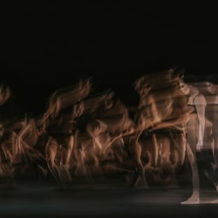 Woman walks across stage with dancers dancing behind her