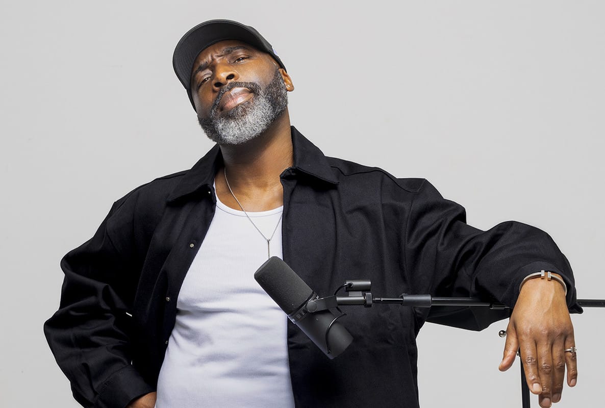 Man in black cap and hoodie leaning on microphone