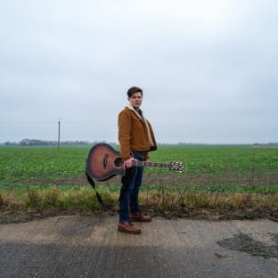 Woman holding acoustic guitar in a field