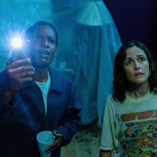 Two people in a dark room looking up holding a flashlight