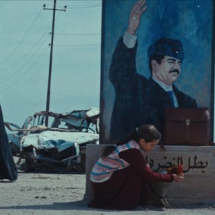 A young girl in front of a poster of Sadam Hussein